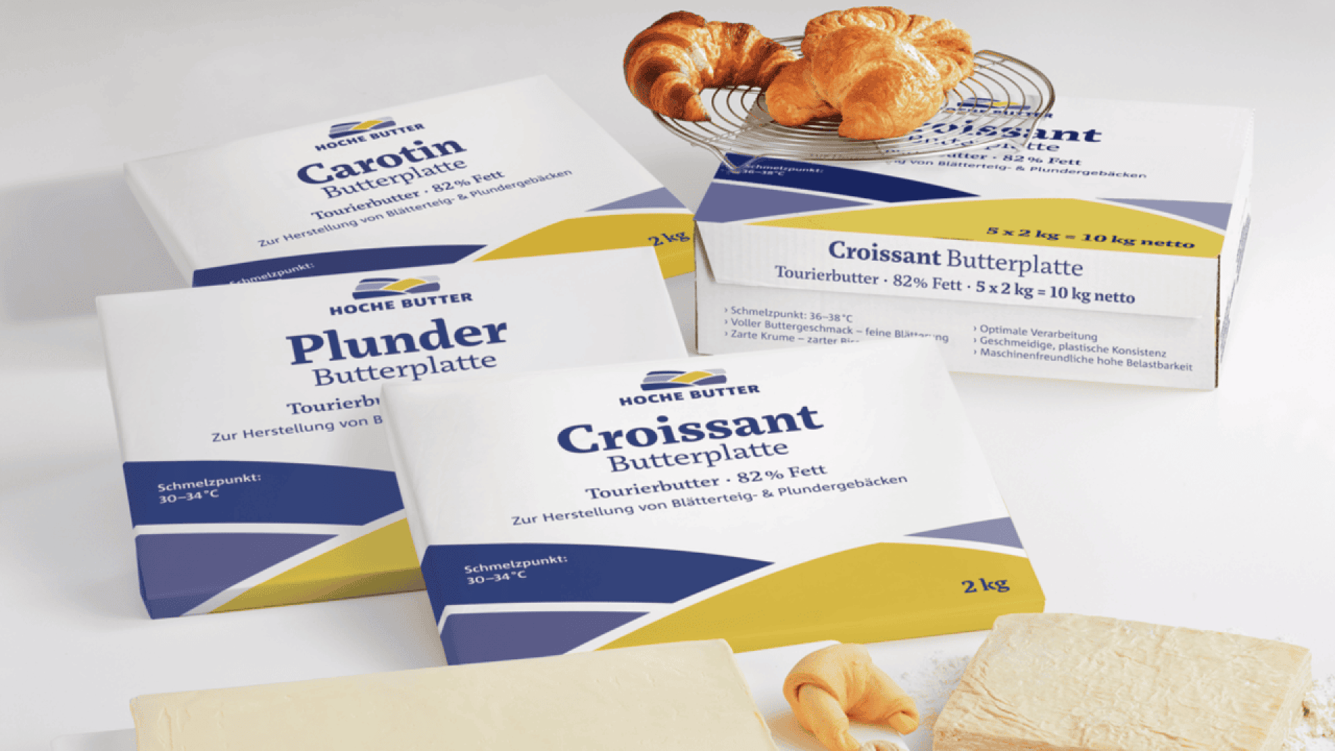 Four packages of Hoche Butter labeled for making croissants and pastries are displayed with croissants, a chunk of butter, and a rolling pin on a white surface. The packages feature blue, yellow, and white designs.