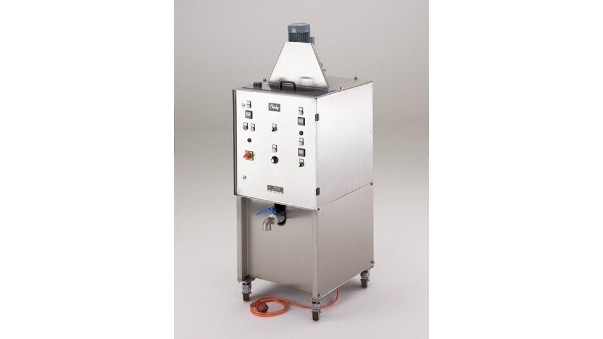 A stainless steel industrial machine with a control panel, buttons, and switches on the front. It stands on four legs and has an orange electrical cord at the base. The background is plain and light-colored.