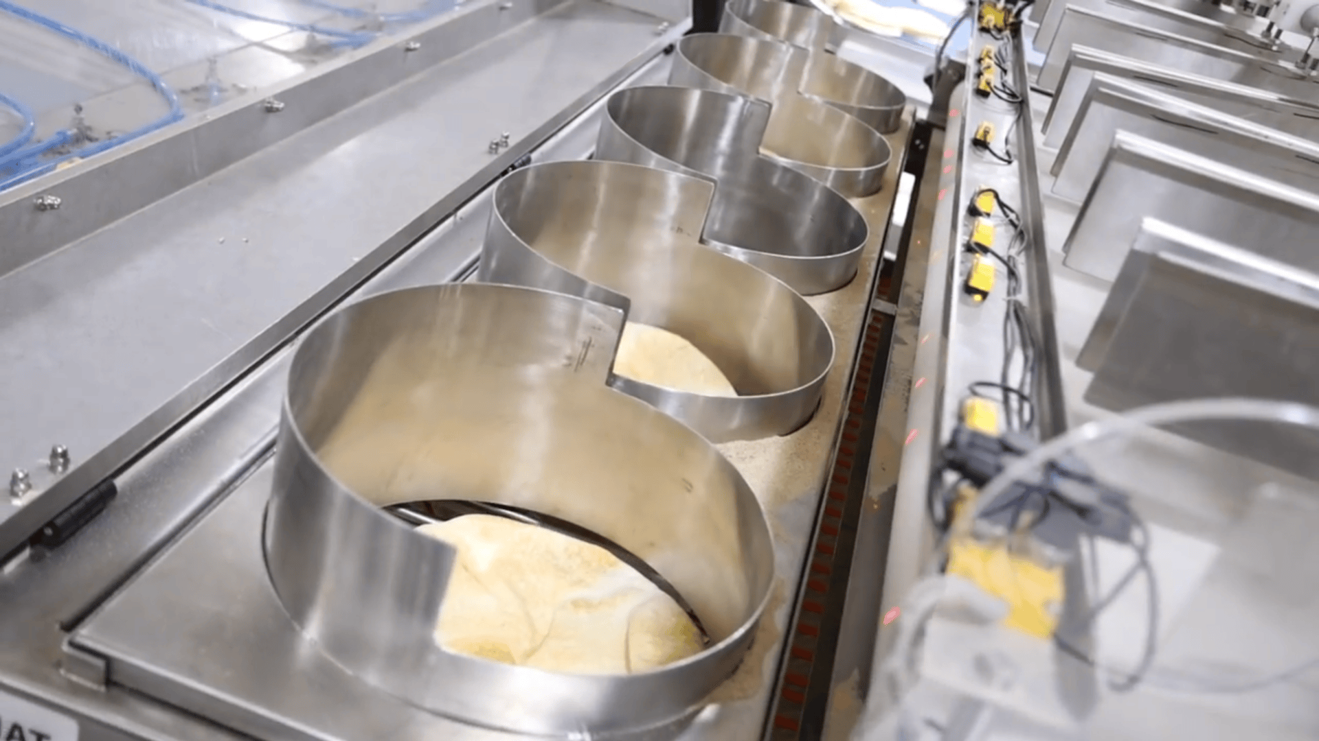 Large metal Mickey Mouse-shaped molds filled with dough are lined up on a conveyor belt in a food production facility.