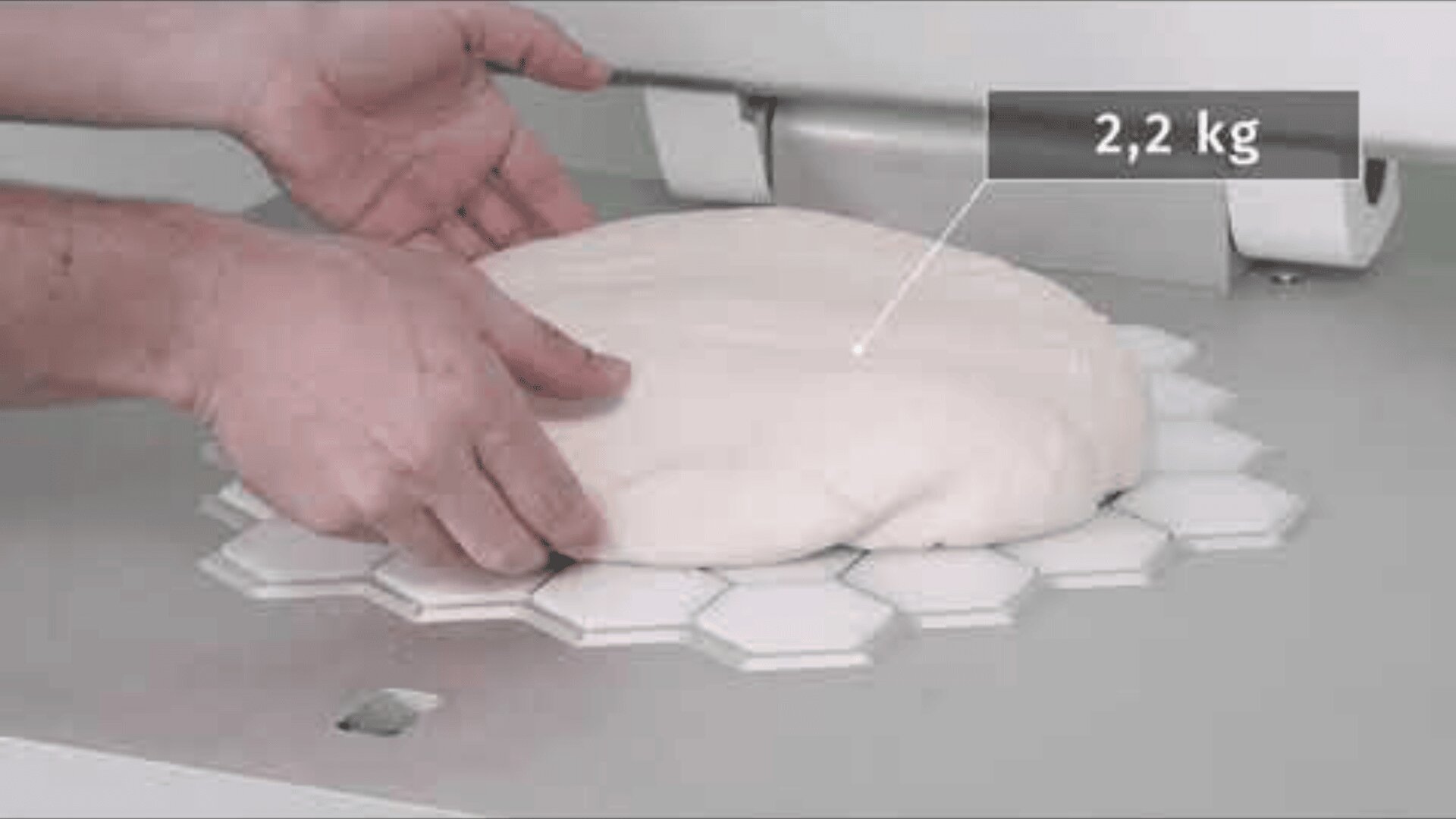 Eine Person legt ein 2,2 kg schweres Teigstück auf eine sechseckige Fläche und bereitet es wahrscheinlich zum Schneiden oder Teilen in einer Großküche vor.