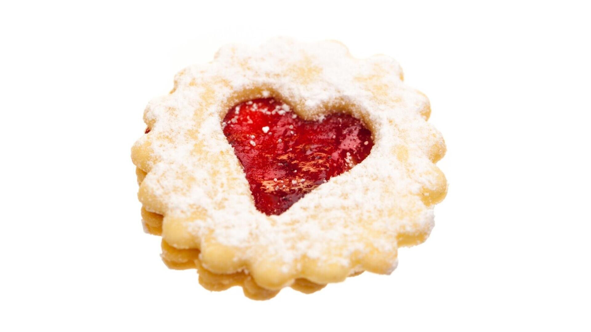 A round, scalloped-edge cookie with a heart-shaped cutout filled with red jam, dusted with powdered sugar, on a white background.