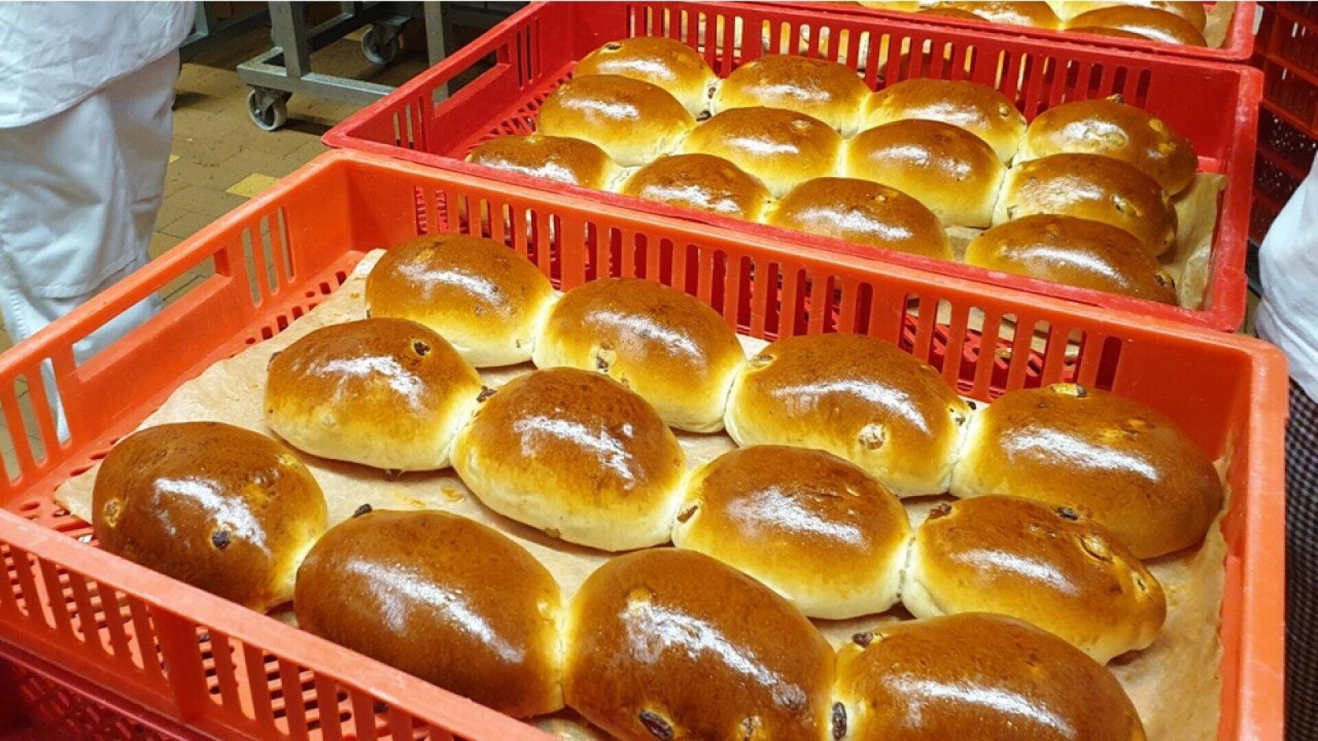 Rows of shiny, golden-brown buns are arranged neatly in red plastic trays lined with parchment paper, ready for packaging or sale in a bakery setting.