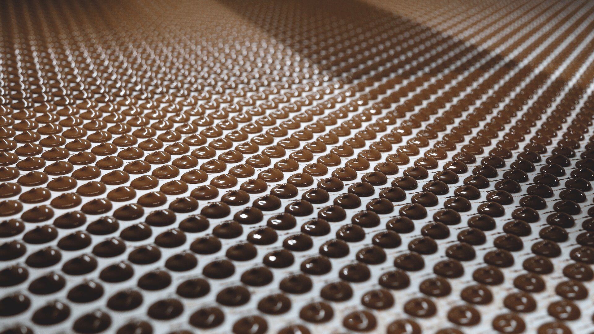 Rows of small, round chocolate drops are arranged in a grid pattern on a flat surface, reflecting light and creating a visually appealing, geometric effect.