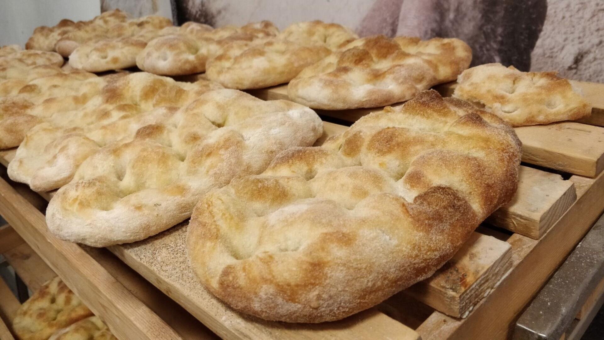 Mehrere Stücke rustikalen, goldbraunen Fladenbrots kühlen auf Holzgestellen ab. Das Brot hat eine leicht aufgeblähte, gewellte Oberfläche mit knusprigen Rändern und ist in einer Bäckerei oder Küche in Reihen angeordnet.