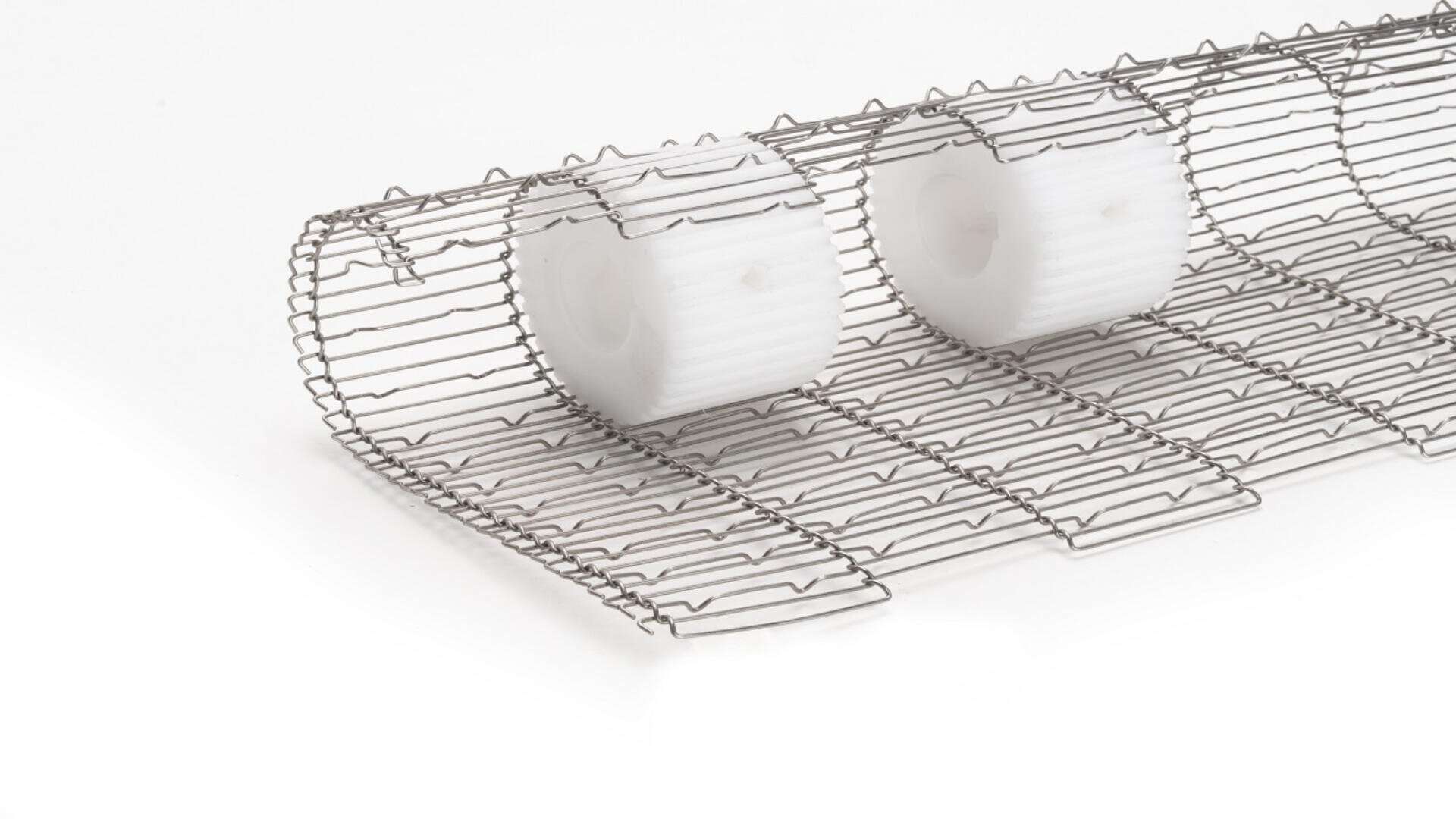 A close-up of a metal wire conveyor belt with two white plastic rollers positioned on top, set against a plain white background.
