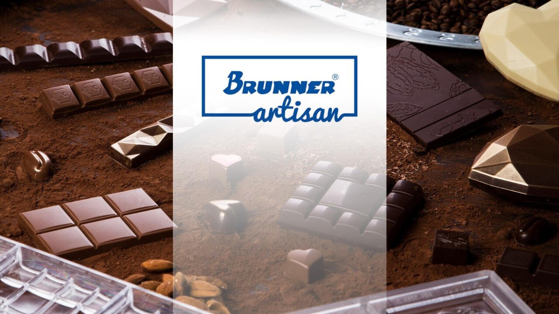 An assortment of artisan chocolates and chocolate bars arranged on a cocoa-dusted surface, with the Brunner Artisan logo displayed in the center over a white translucent strip.