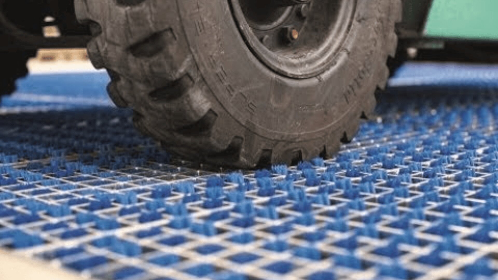Eine Nahaufnahme eines Gabelstaplerreifens, der über ein blaues Anti-Rutsch-Bodengitter mit erhabenen Spikes rollt, das für Traktion und Sicherheit in industriellen Umgebungen konzipiert ist.