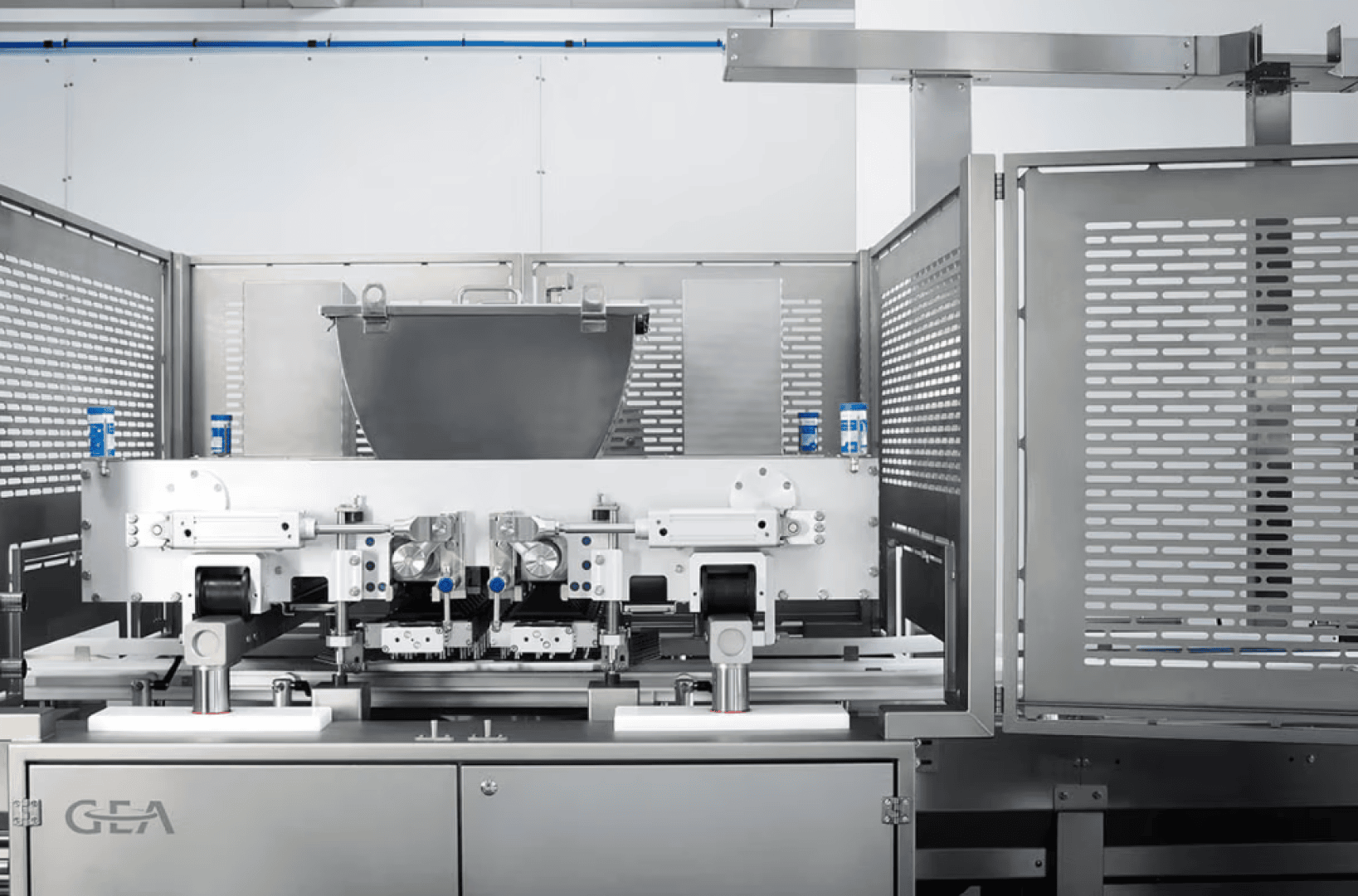 Eine moderne industrielle Verpackungsmaschine mit Edelstahlpaneelen und einem großen zentralen Trichter, flankiert von blauen Sensoren, steht in einer sauberen, weißen, automatisierten Produktionsanlage.