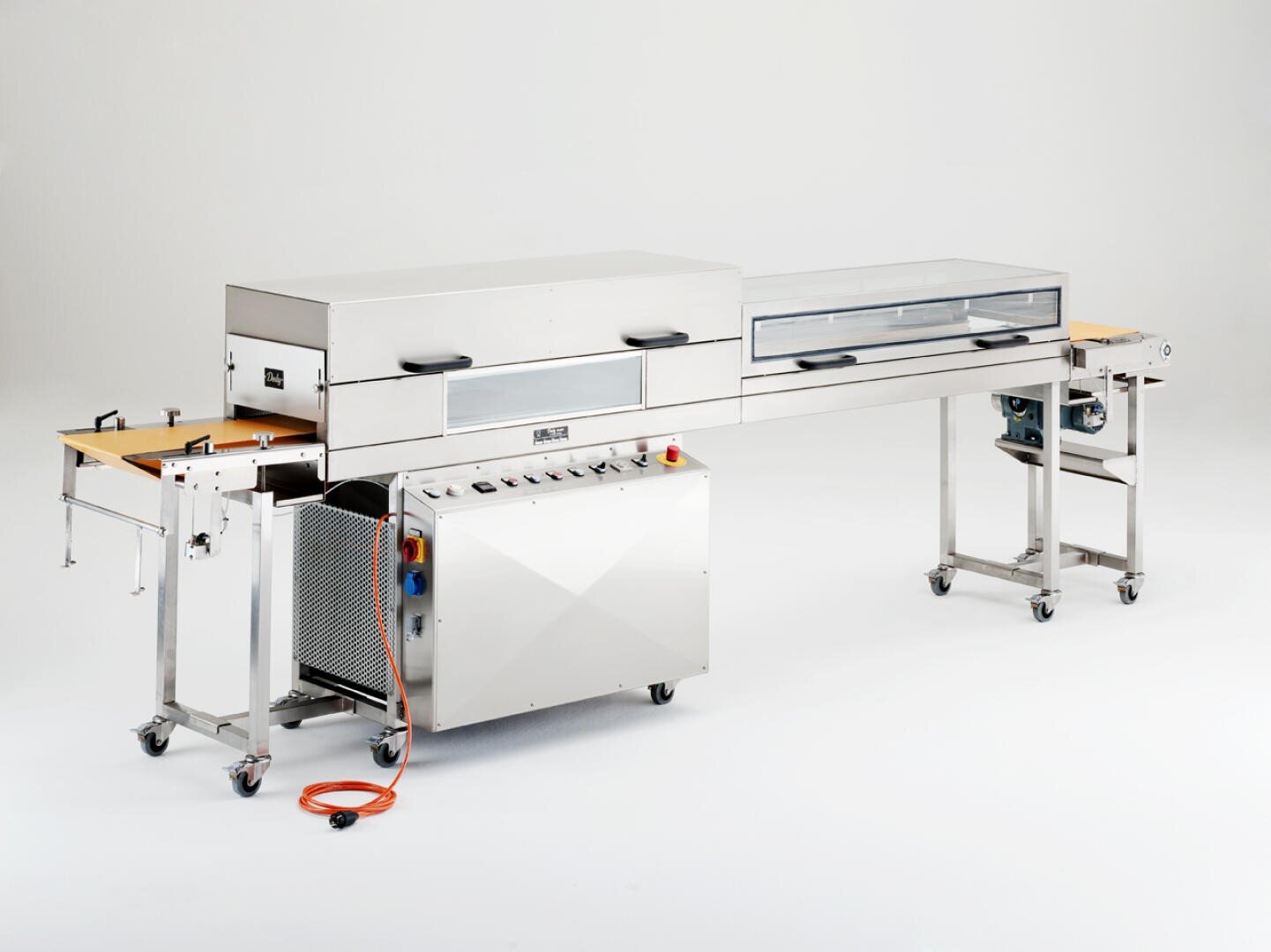 Eine große industrielle Lebensmittelverarbeitungsmaschine mit einem Förderband, einem Bedienfeld und einem Gehäuse aus Edelstahl vor einem schlichten weißen Hintergrund. Auf dem Boden ist ein orangefarbenes Stromkabel zu sehen.