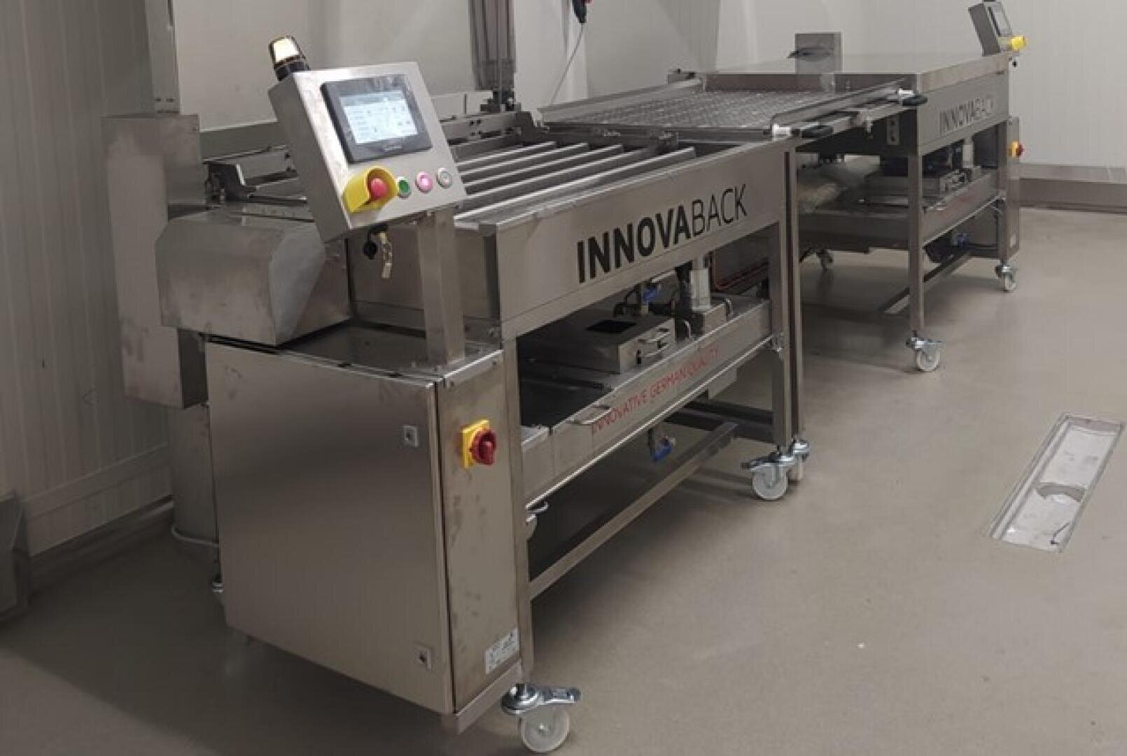 Industrielle Lebensmittelverarbeitungsmaschinen aus Edelstahl mit der Bezeichnung INNOVABACK, mit Schalttafeln und Rollen, die auf einem sauberen Fabrikboden stehen.