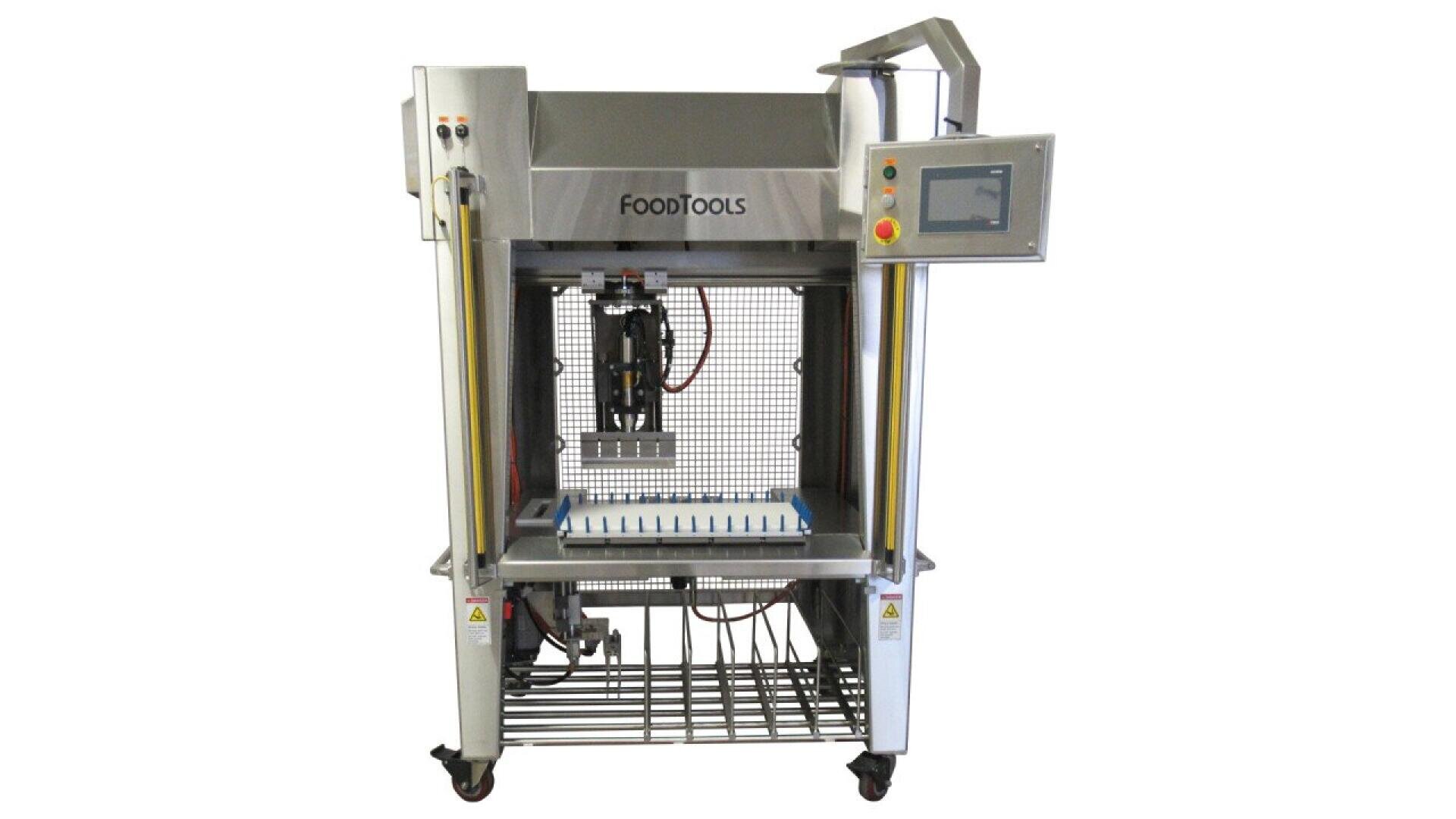 Eine industrielle Lebensmittelverarbeitungsmaschine aus Edelstahl mit Digitalanzeige und der Aufschrift FOODTOOLS, die zum automatischen Schneiden oder Portionieren bestimmt ist und auf Rädern mit einem Metallgestell darunter steht.