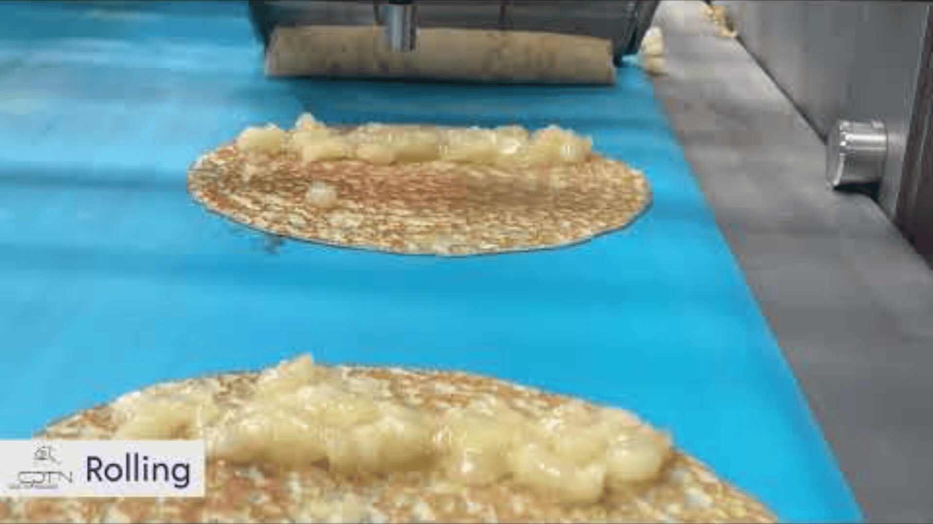 A machine spreads filling onto flat crepes on a blue conveyor belt in a food production line. The word Rolling appears in the lower left corner.