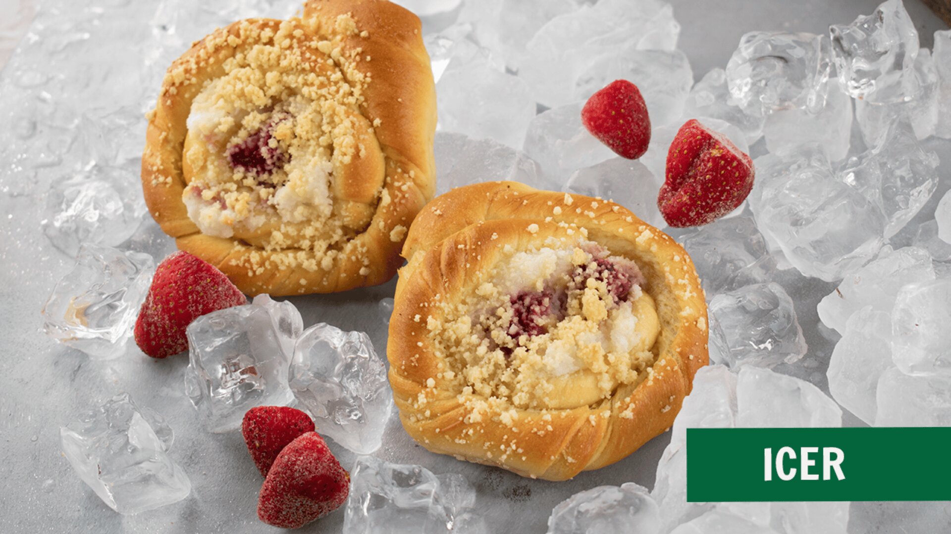 Two pastries with crumb topping and fruit filling are placed on a surface with ice cubes and frozen strawberries scattered around them. A green label at the bottom right corner reads ICER.