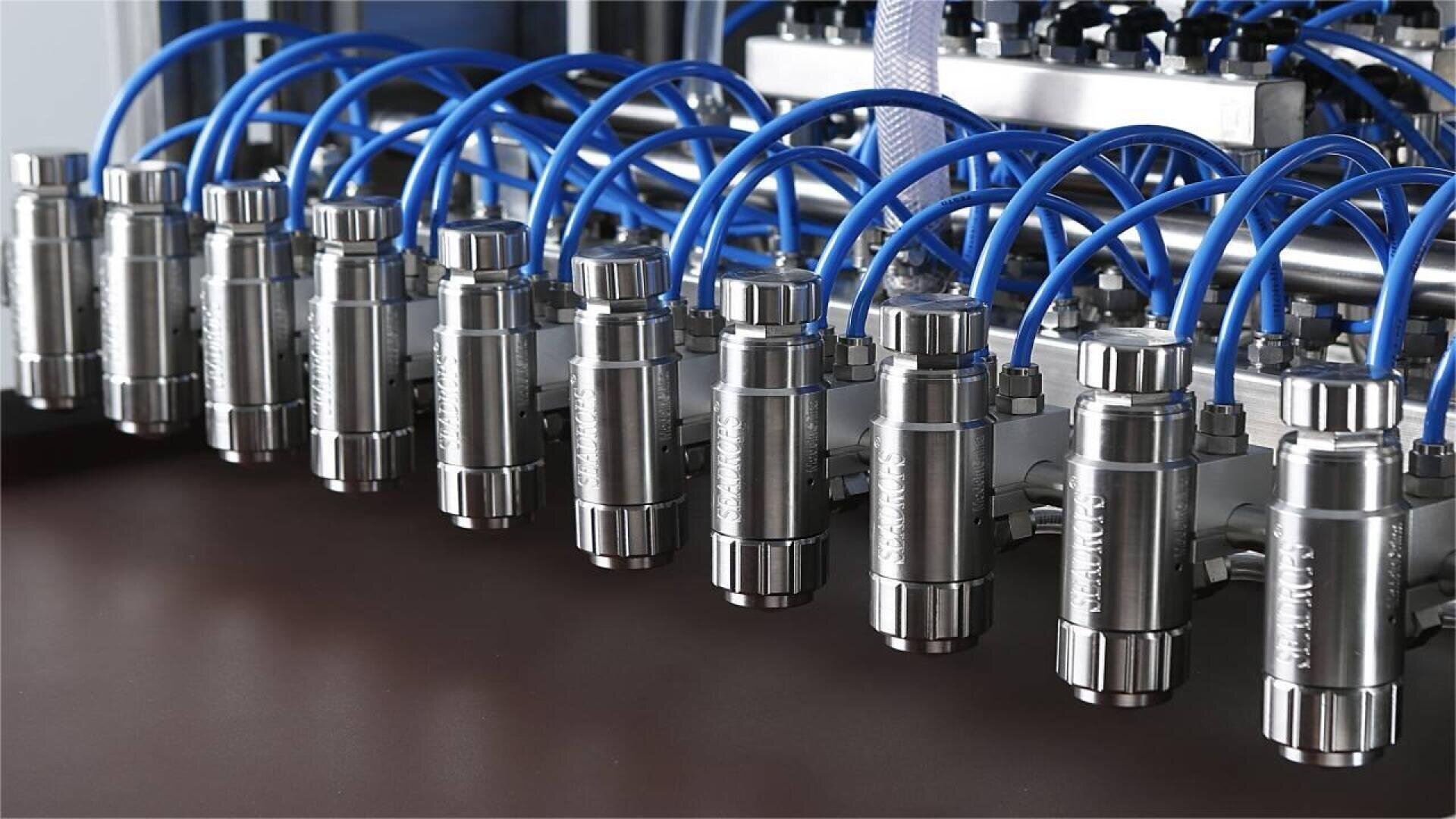 A close-up view of a row of metal industrial valves connected by blue tubing, likely part of an automated manufacturing or fluid control system.