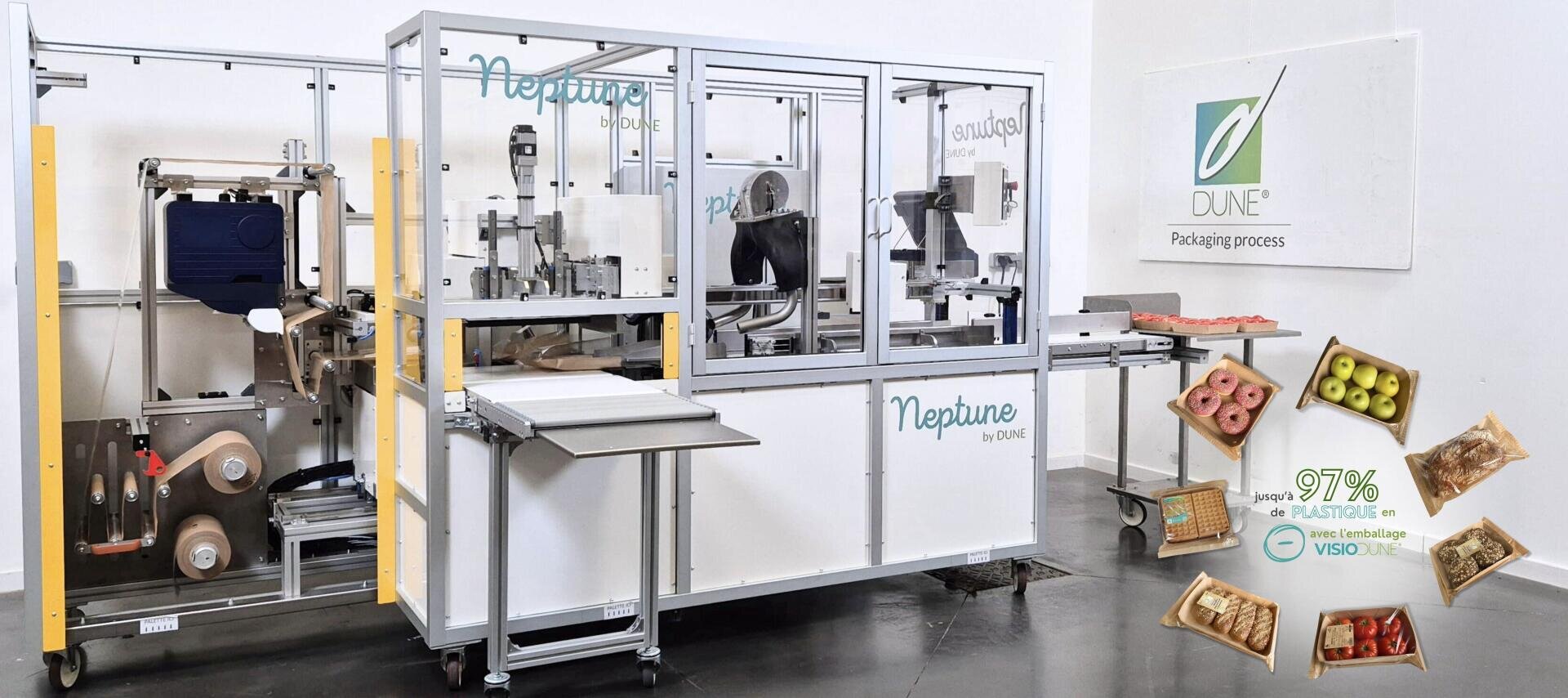 A white industrial packaging machine labeled Neptune by DUNE stands in a clean room. On the wall is a DUNE logo. Packaged food samples and a label highlighting “97% PLAntiful” are displayed on the right.
