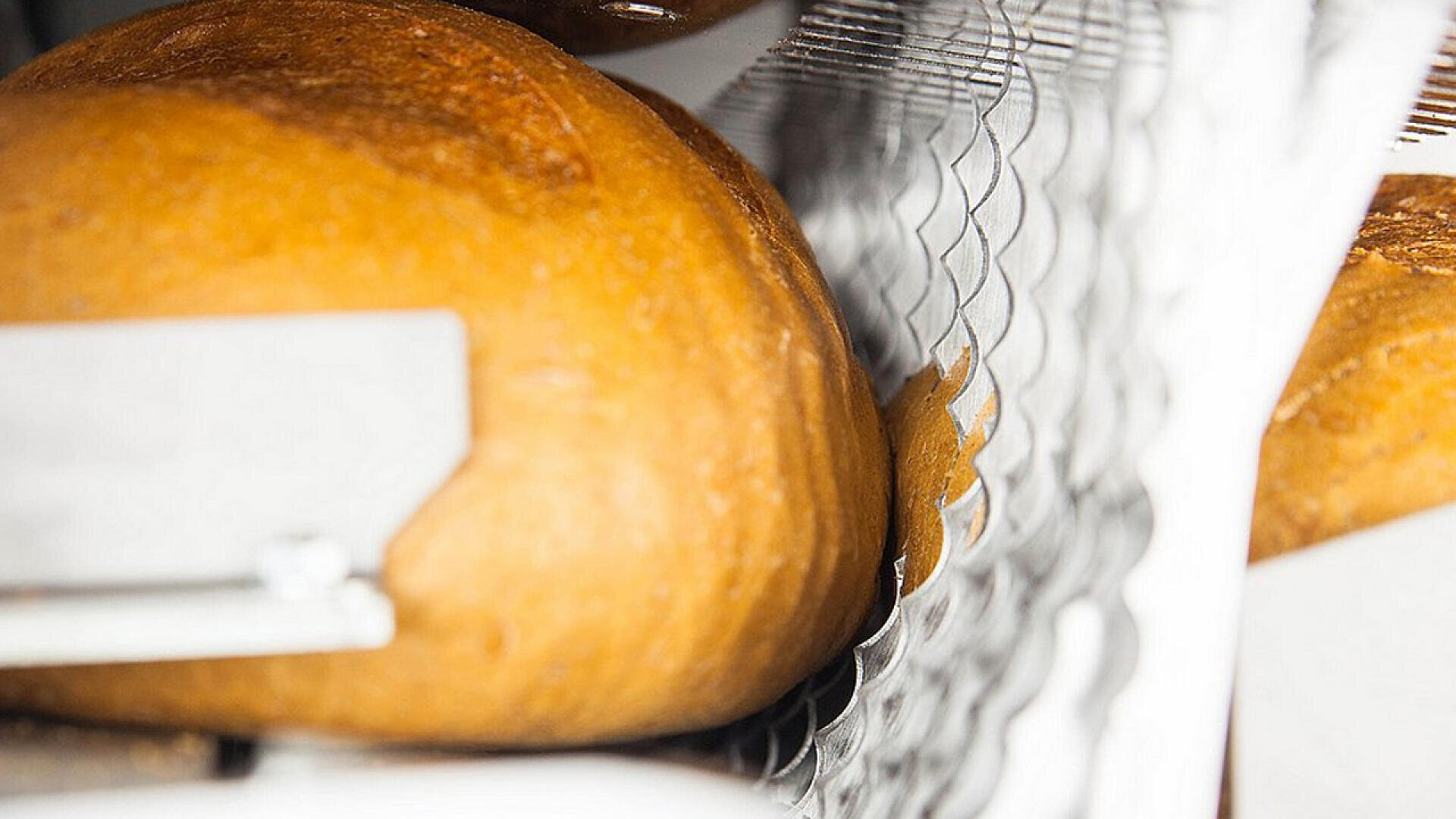 A close-up view of a loaf of bread being sliced by a metal wire mechanism in an industrial bread slicing machine.