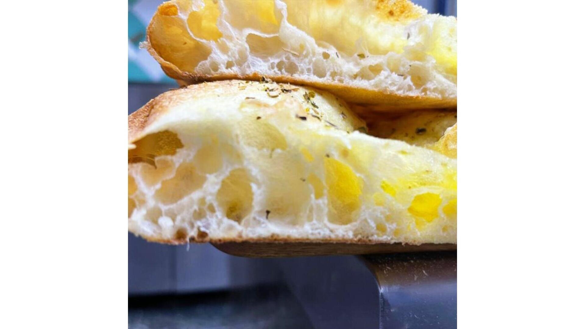 Nahaufnahme von luftigen, goldenen Focaccia-Brotscheiben, die übereinander gestapelt sind. Sie zeigen ein leichtes, fluffiges Inneres mit sichtbaren Lufteinschlüssen und eine leicht knusprige, goldene Kruste.