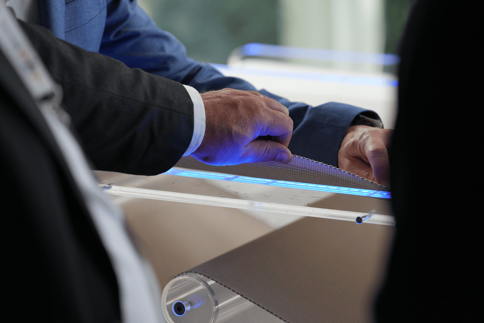 A close-up of two people in business attire examining a textured sheet of material under a blue light, with one person touching the material and the other observing.