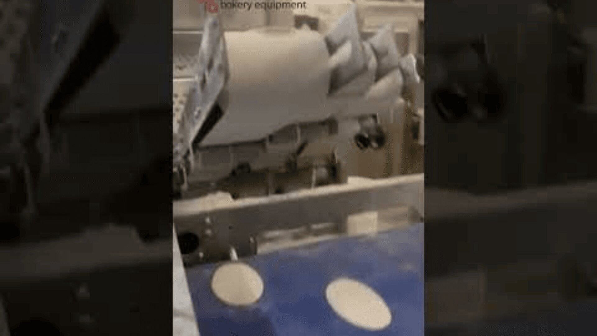 A dough machine automatically cuts round shapes out of flat dough sheets, placing them onto a blue conveyor belt as part of an industrial bakery process.