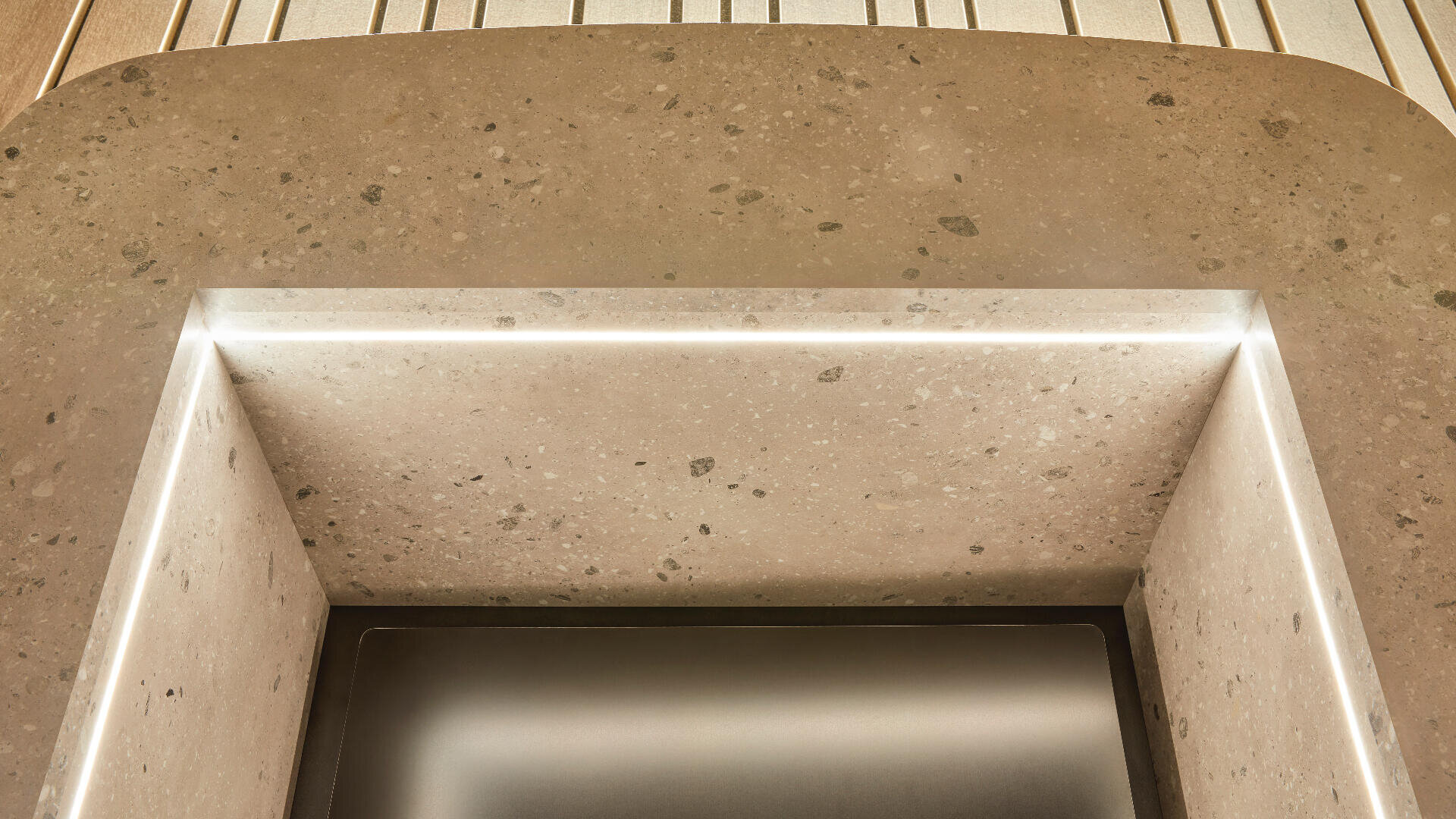 Nahaufnahme eines modernen, rechteckigen Steinwaschbeckens mit abgerundeten Kanten und integrierter LED-Beleuchtung entlang des inneren Randes vor einem Hintergrund aus heller Holzverkleidung.