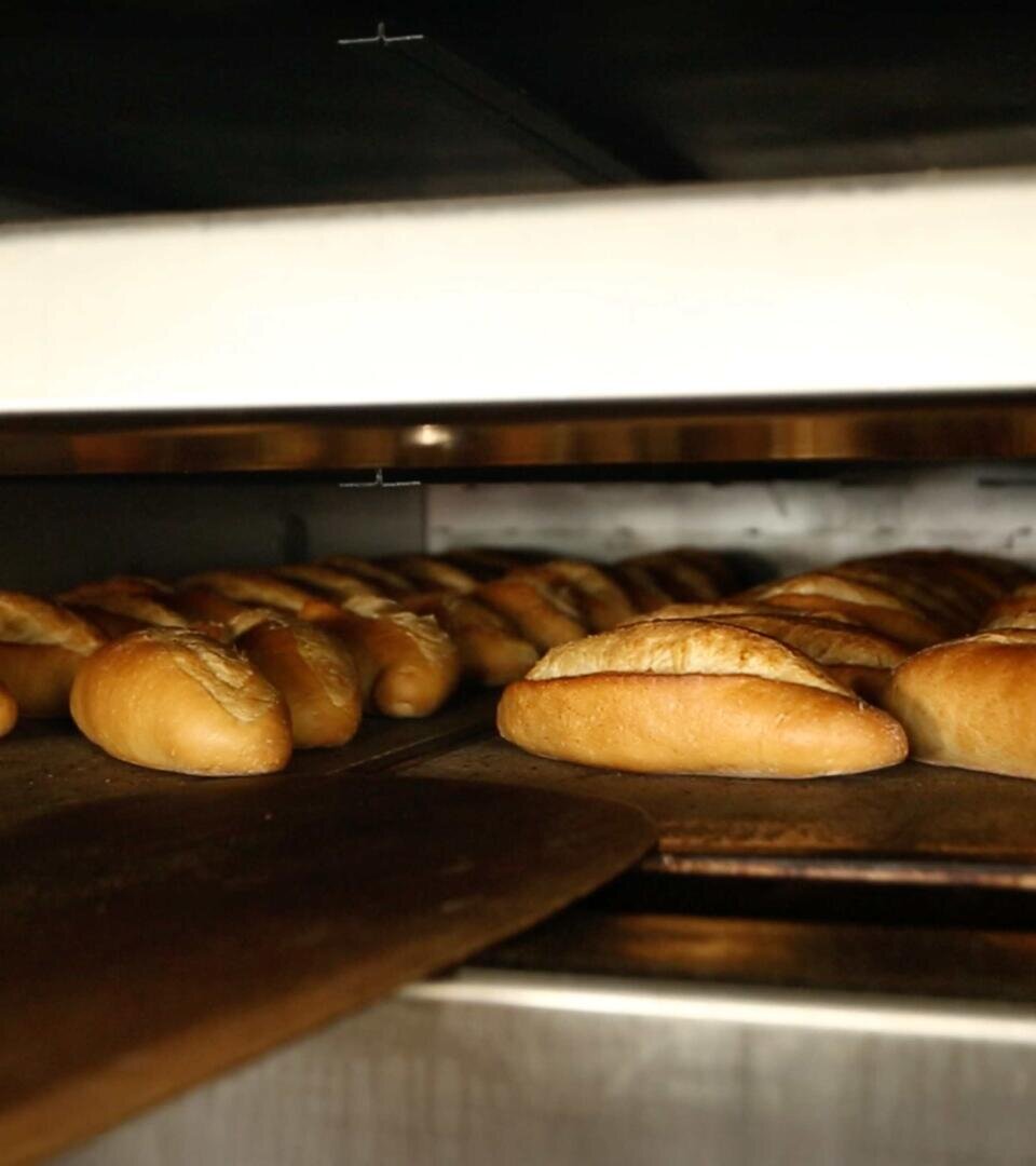 In a large industrial oven, rows of golden brown rolls are baked on metal trays, their crispy crusts highlighted by the warm light.