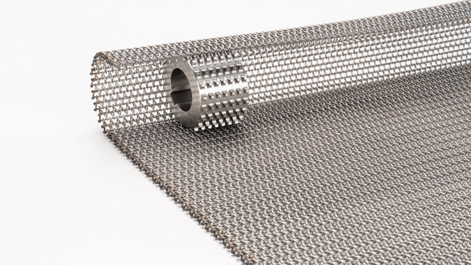 A roll of metal wire mesh is partially unrolled on a white surface, showing its grid-like pattern and sturdy woven texture.