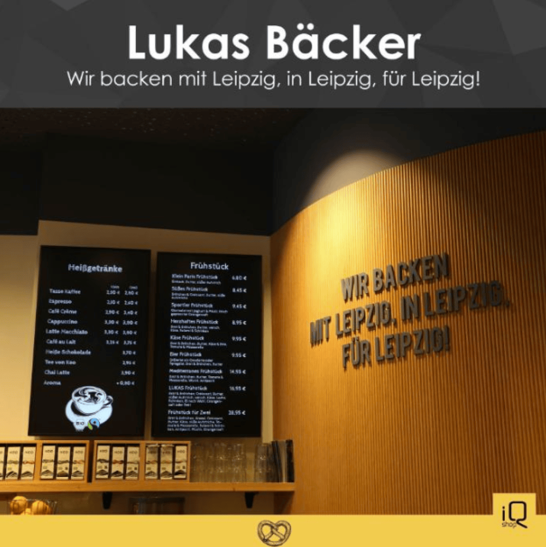 Das Innere eines Cafés, links eine Speisekarte mit Getränken und Frühstücksangeboten, rechts eine Holzwand mit der Aufschrift Wir backen mit Leipzig, in Leipzig, für Leipzig!.