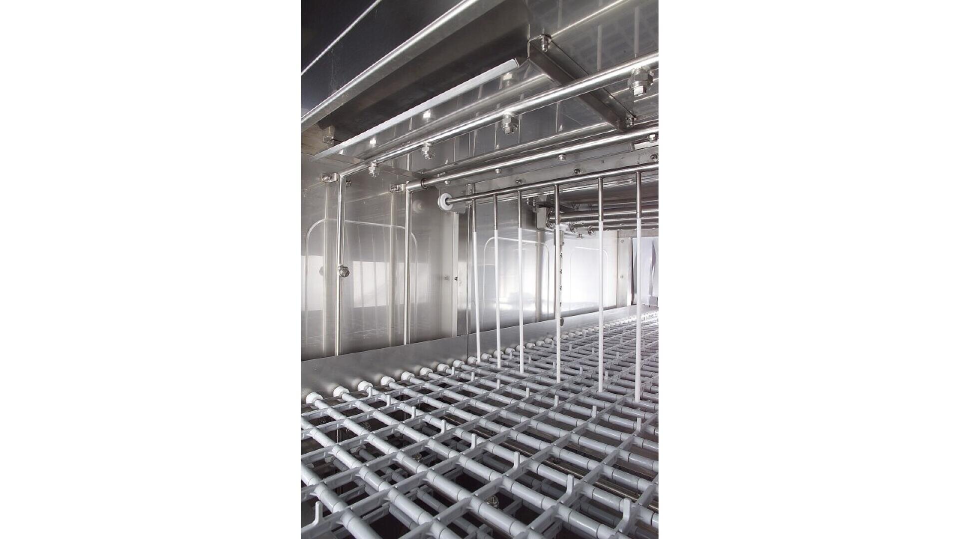 Nahaufnahme des Inneren einer Industriemaschine aus Edelstahl. Zu sehen sind eine Reihe parallel angeordneter Rohre, Stangen und Rollen, die wahrscheinlich für die automatisierte Verarbeitung oder Herstellung verwendet werden.