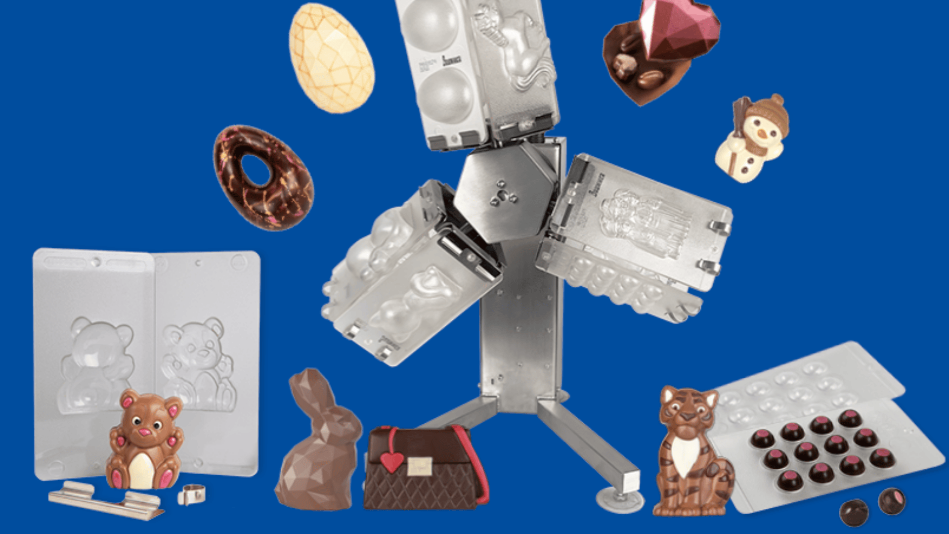 Eine Vielzahl von Schokoladenformen und Pralinen in Form von Bären, Hasen, Herzen, Eiern und Handtaschen sind um eine zentrale rotierende Schokoladenformmaschine auf blauem Hintergrund ausgestellt.