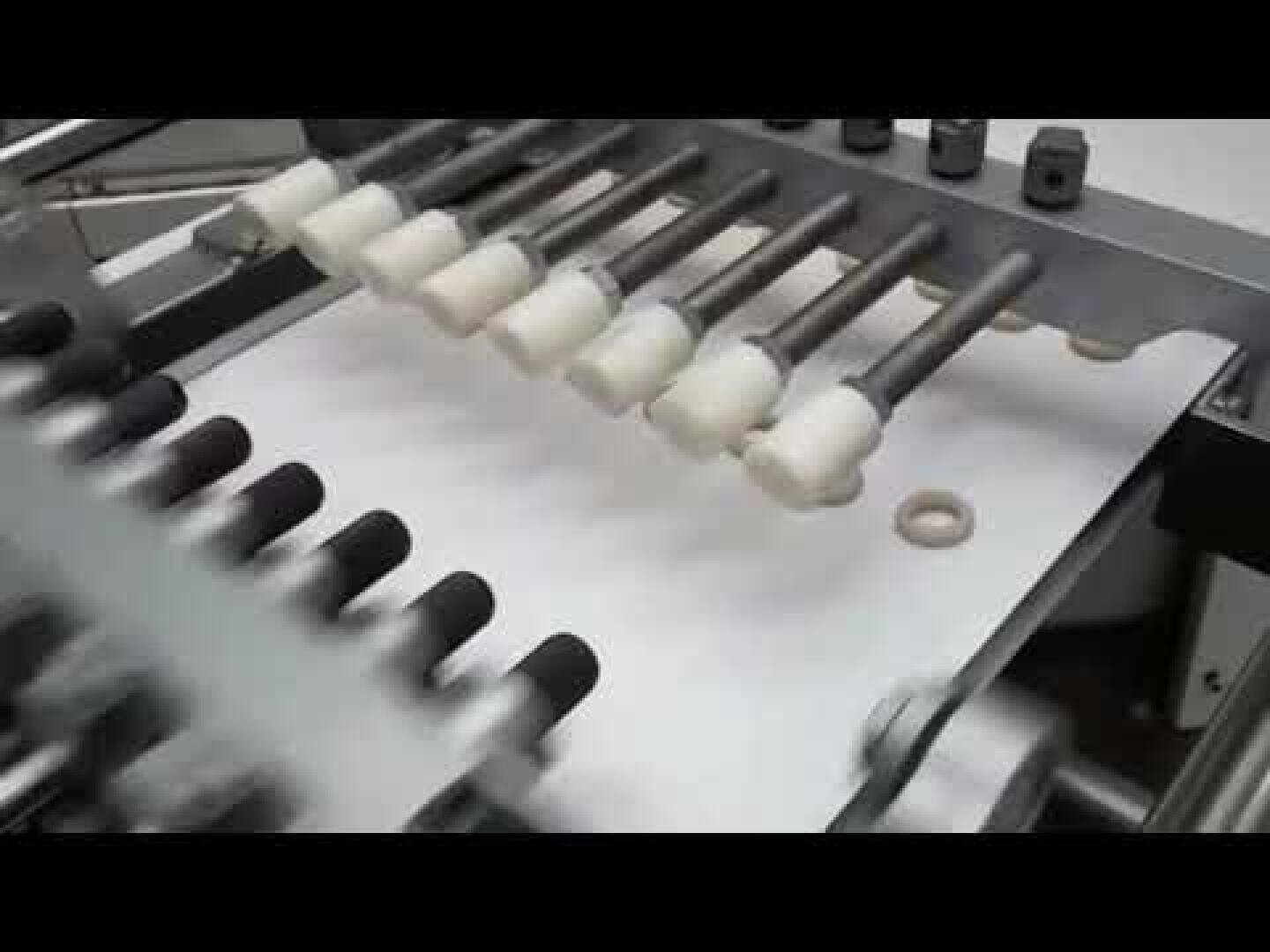 A close-up of a machine with multiple metal rods sorting small, circular beige objects onto a white conveyor belt in an industrial setting.
