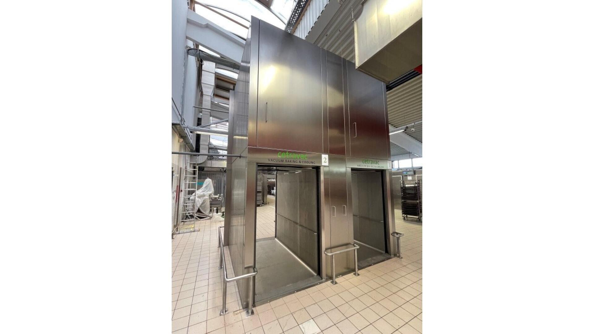 Große begehbare Edelstahl-Reinigungsstation in einer Industrieanlage mit gefliesten Böden, hohen Decken und Metallgeländern auf beiden Seiten der Eingänge.