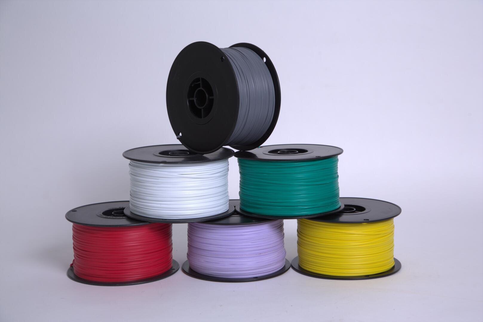 Six spools of 3D printer filament in red, white, gray, green, purple, and yellow are stacked in two tiers against a plain white background. The gray spool is on top, with the others arranged below it.