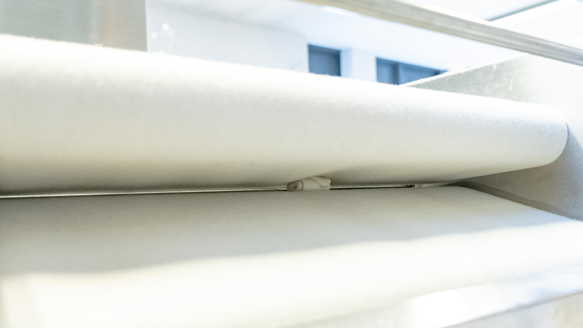 A small piece of dough is being rolled between two large sheets of white fabric in a brightly lit industrial setting.