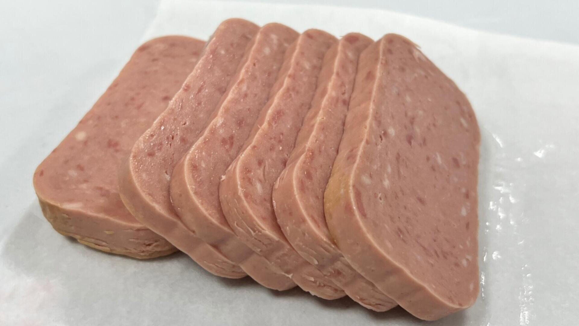 Sechs Scheiben Frühstücksfleisch, z. B. Dosenfleisch, werden in einer leicht überlappenden Reihe auf einem Stück weißem Pergament- oder Wachspapier angeordnet.