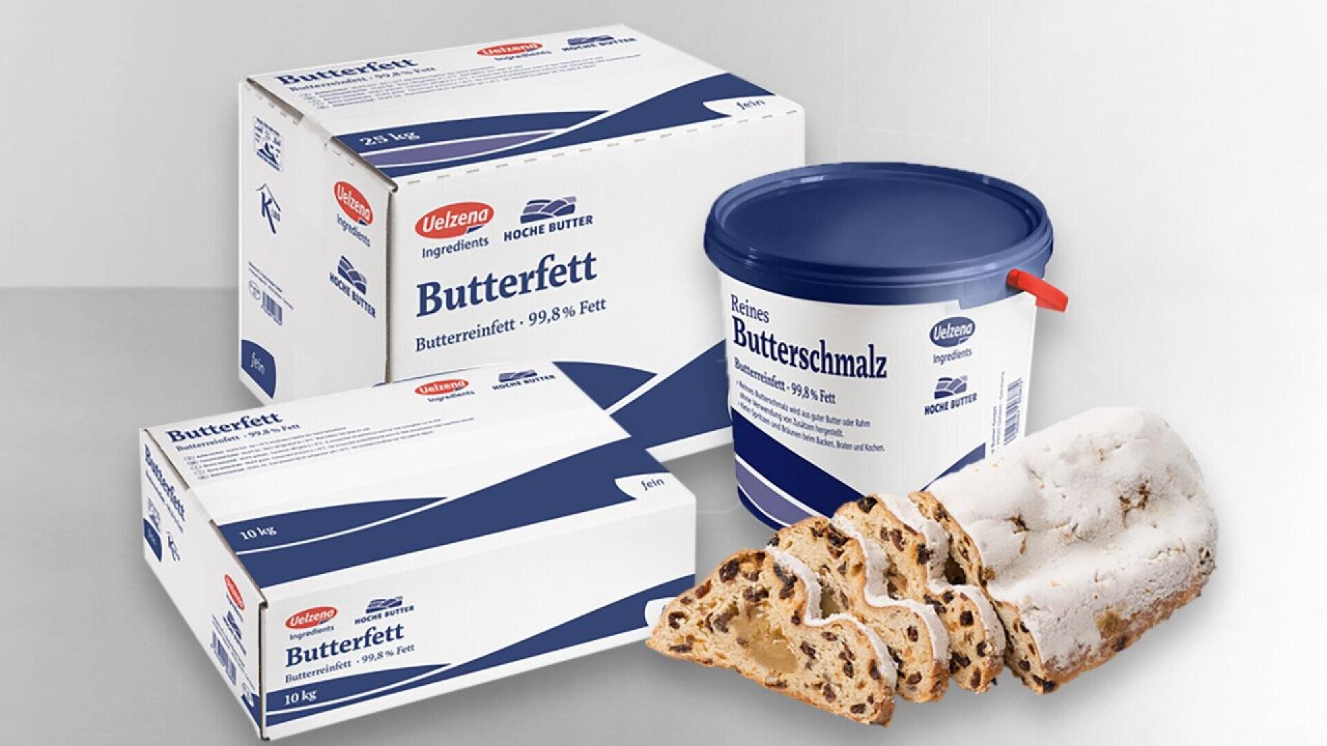 Three packages of German butterfat and clarified butter are displayed next to several slices of stollen, a traditional fruit bread dusted with powdered sugar. The packages are white with blue text and accents.