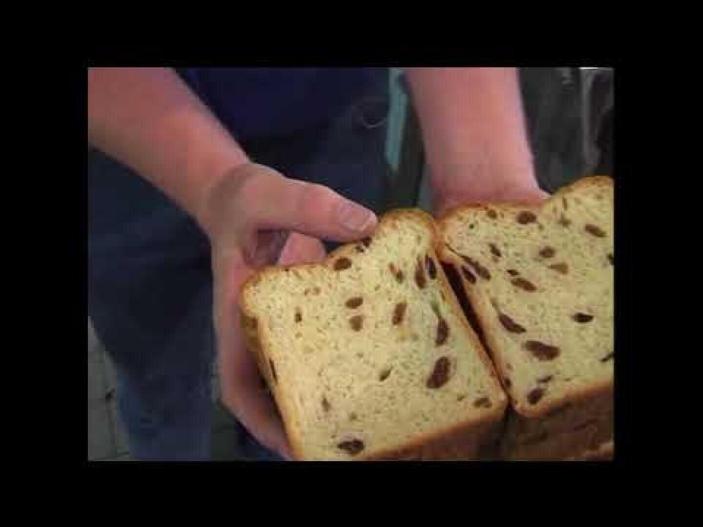 A person holds two slices of raisin bread, one in each hand, showing the inside with visible raisins. The image has a black border around it.