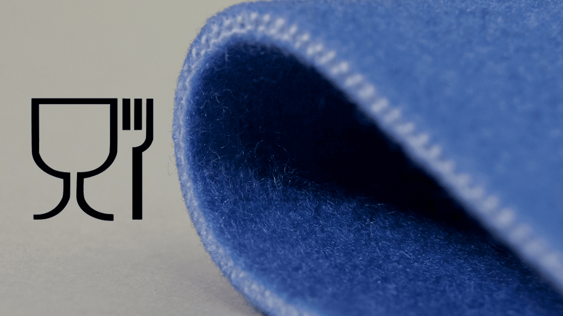 Eine Nahaufnahme eines blauen Stoffes mit gewelltem Rand, abgebildet neben dem Symbol für Lebensmittelsicherheit, das ein Trinkglas und eine Gabel zeigt.
