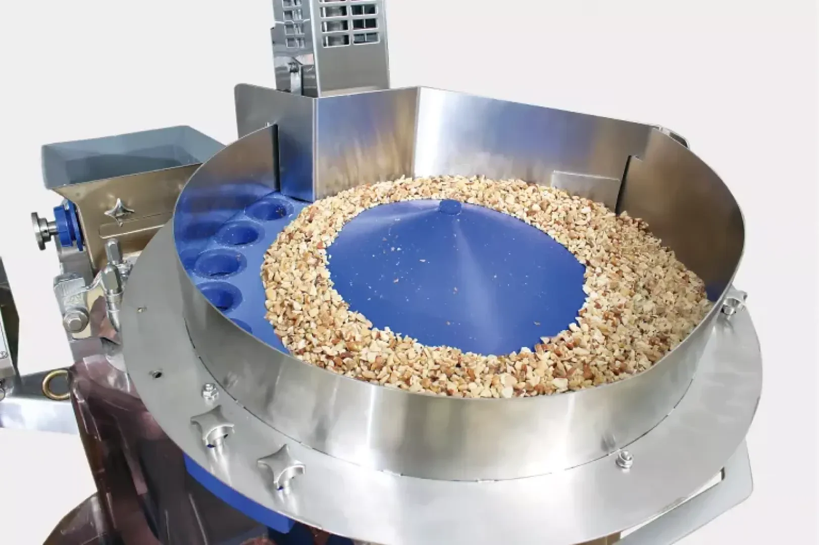 A stainless steel industrial machine with a blue circular tray sorting chopped nuts, likely used for food processing or packaging.