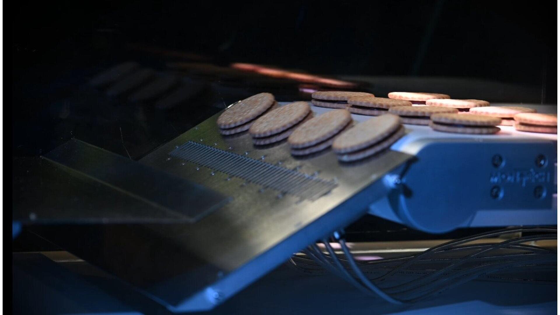 A close-up of several sandwich cookies being transported on a conveyor belt in a factory or industrial setting.