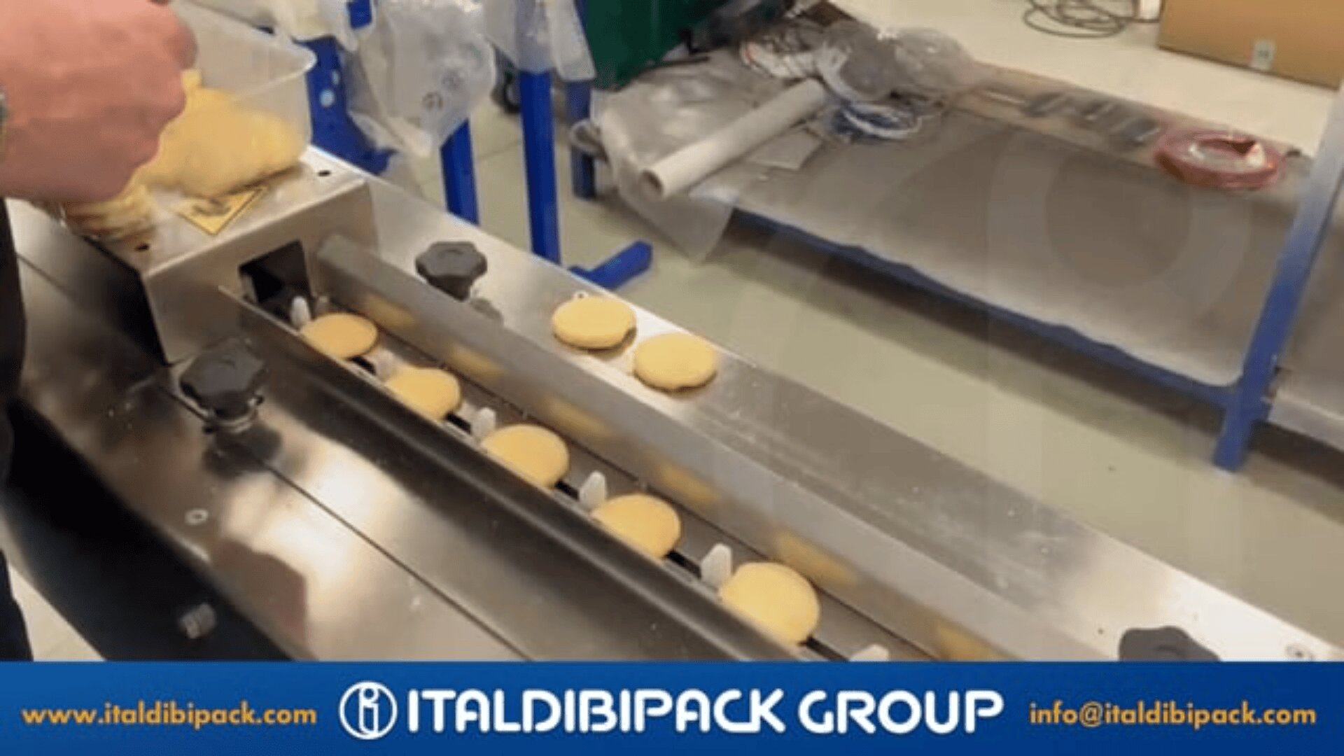 A person places round cookies onto a conveyor belt packaging machine in a factory setting. The image includes the ItalDibipack Group logo and website at the bottom.