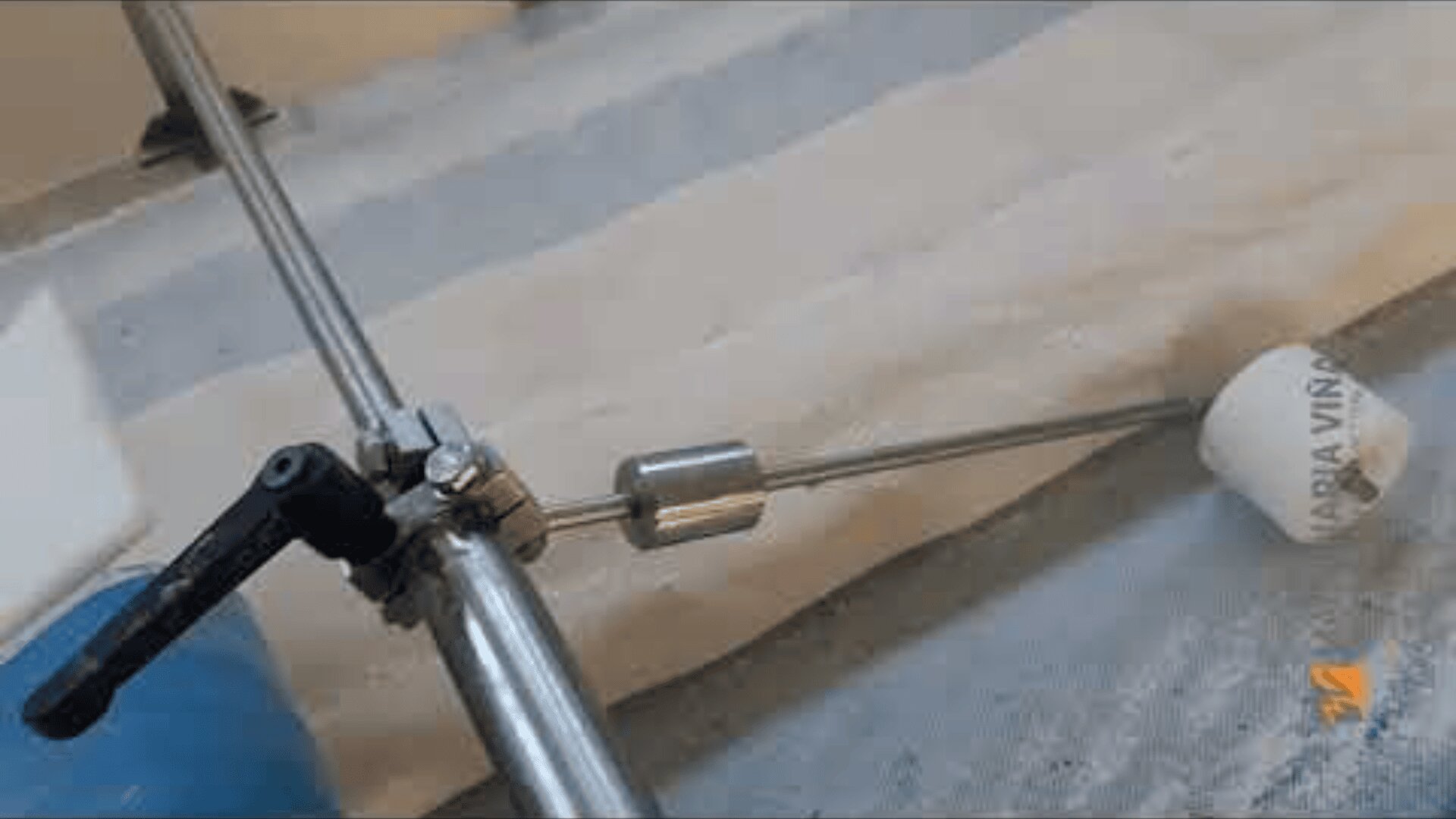 A metal tool with a cylindrical roller and a handle is positioned over a sheet of dough on a work surface. The tool is apparently used to flatten or shape the dough.