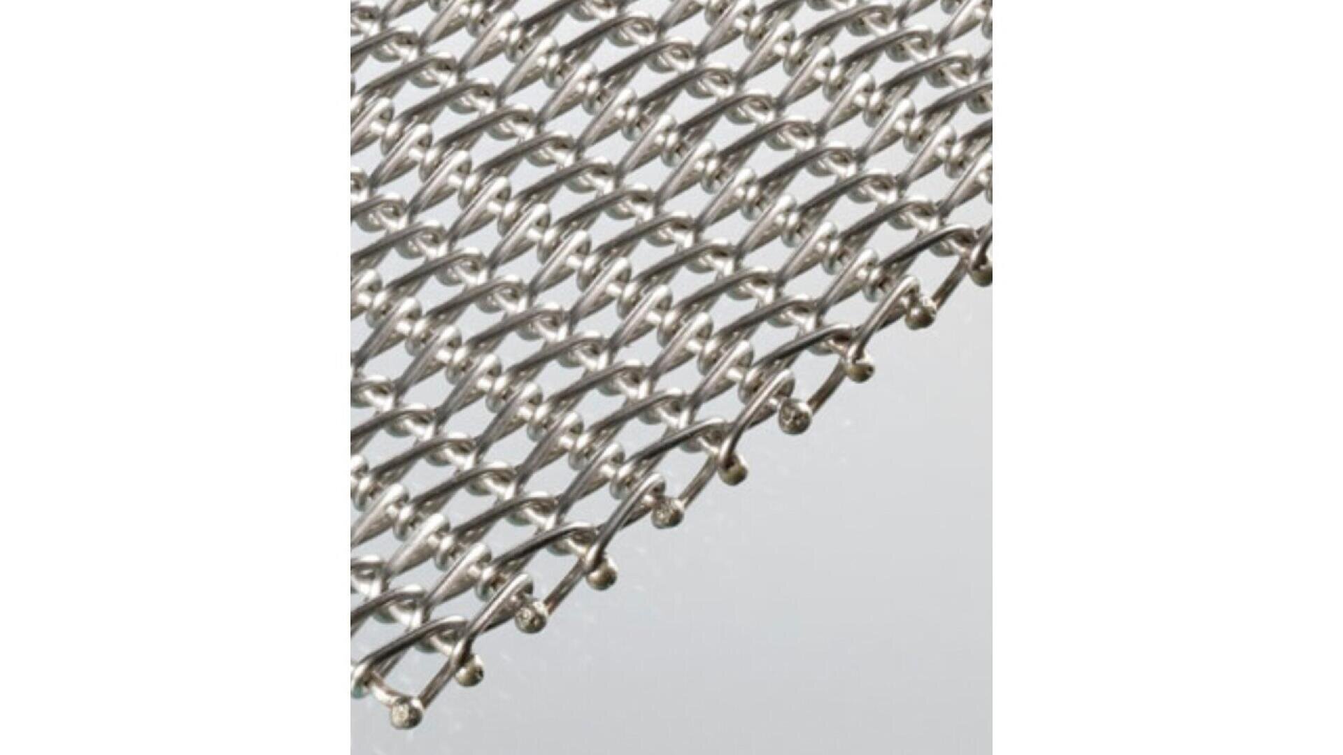 Close-up view of a metallic mesh or wire fabric with a repeating, interlocking loop pattern, photographed against a plain light background.