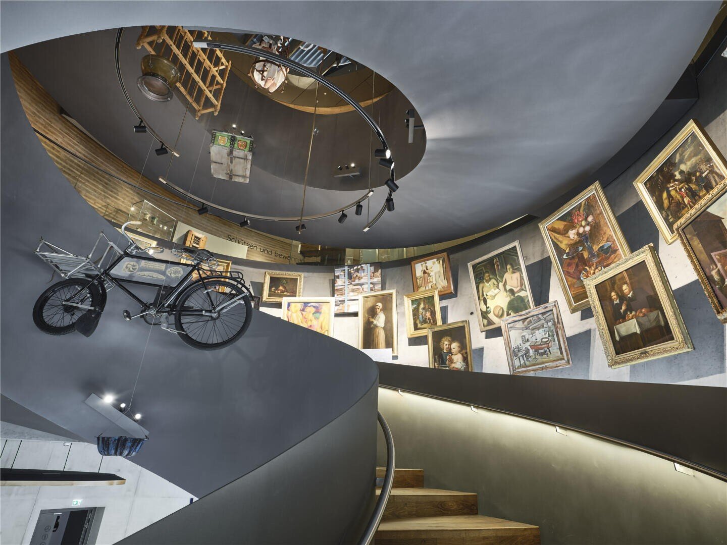 Eine moderne Wendeltreppe mit gerahmten Gemälden an den Wänden und einem darüber montierten alten Fahrrad. An der Decke befinden sich runde Spiegel, die das eklektische, galerieartige Interieur widerspiegeln.