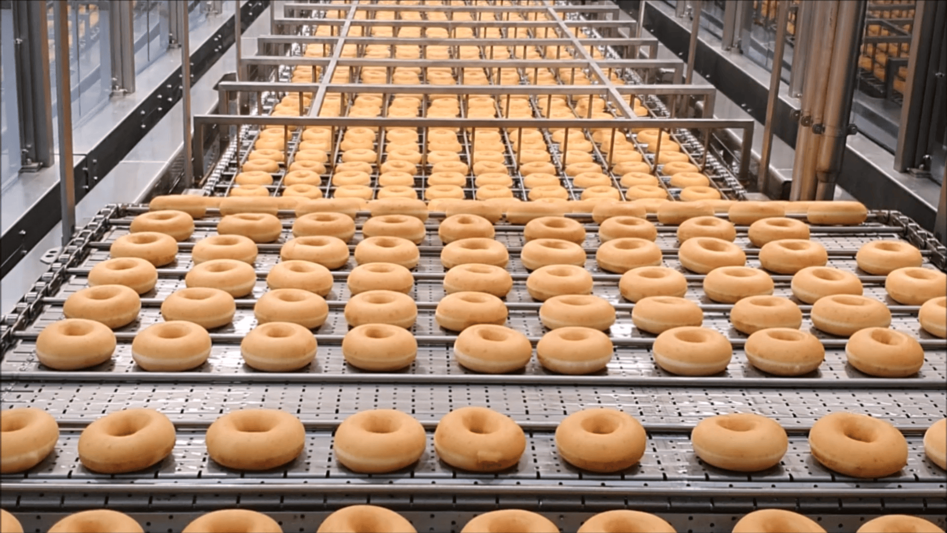 In einer großen Fabrik laufen Reihen einfacher Donuts über ein Fließband und zeigen die Massenproduktion in einer hell erleuchteten, modernen Anlage.