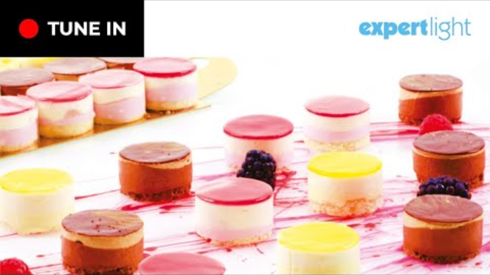 Eine Auswahl bunter Mini-Schichtkuchen mit glänzender Oberfläche, arrangiert auf einer weißen Oberfläche mit Beerengarnitur. In den Ecken erscheinen die Logos für TUNE IN und Expert Light.