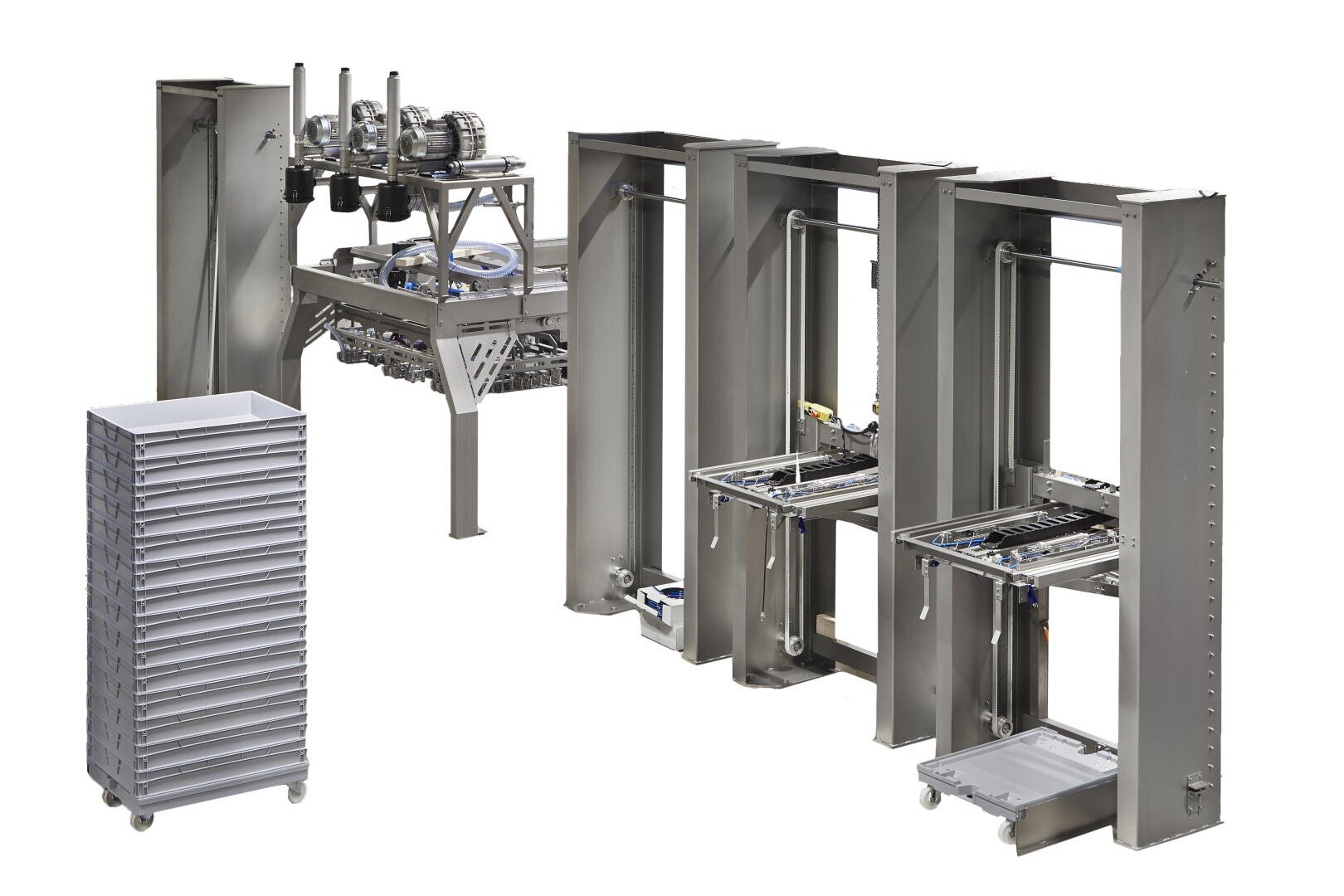 Eine Industriemaschine aus Edelstahl mit drei vertikalen Säulen, mechanischen Komponenten und einem Stapel grauer Tabletts auf Rädern vor einem weißen Hintergrund.