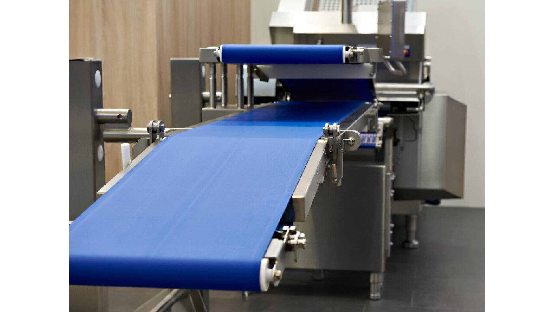 A close-up of an industrial conveyor belt system with a blue belt, stainless steel frame, and machinery in a clean, modern facility.