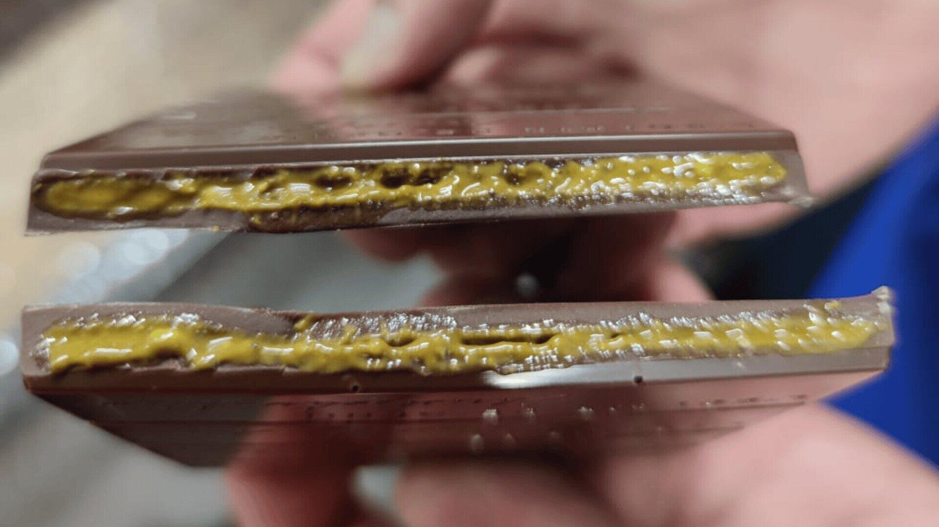 A close-up of two hands holding pieces of chocolate bars split in half, revealing a gooey, yellowish caramel-like filling inside.