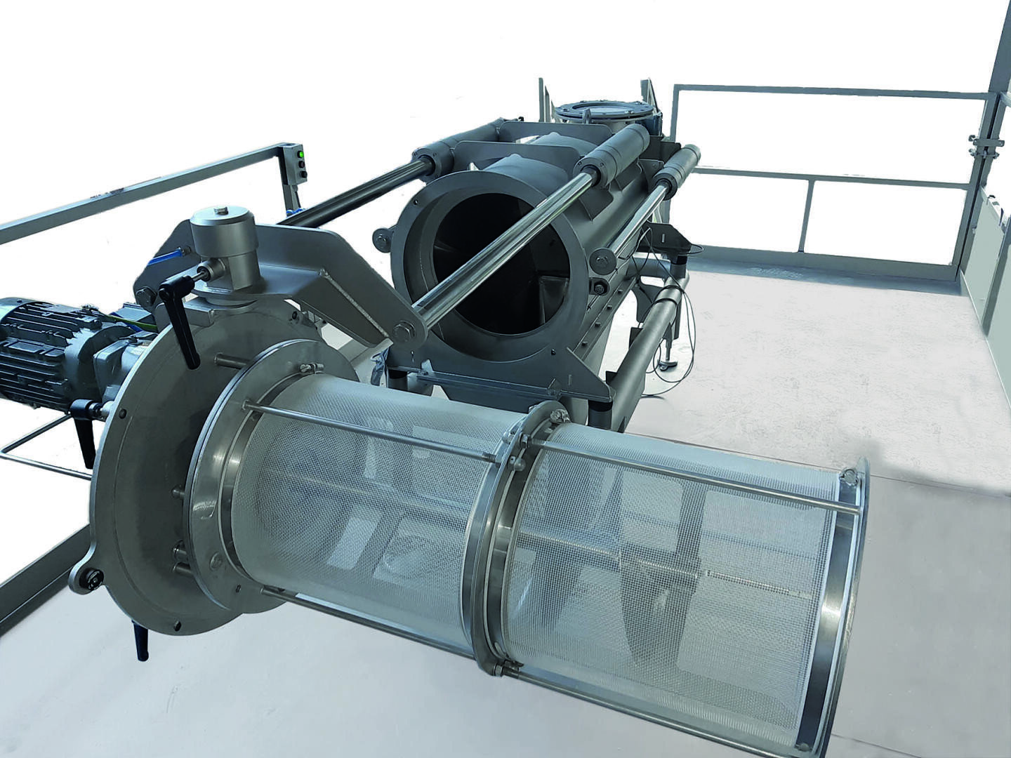 Große Industriemaschine mit einem zylindrischen Metallfilterelement und einem Maschensieb, die auf einer Plattform mit Geländern und Schalttafeln steht und zur Verarbeitung oder Filtration in einer Fabrik verwendet wird.