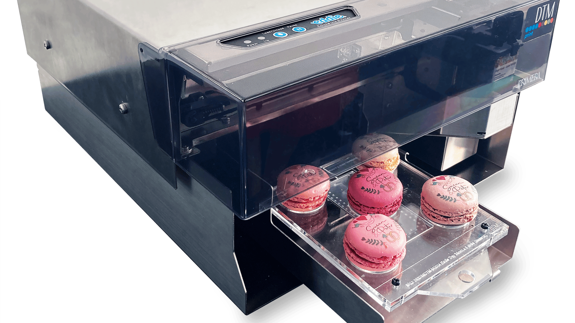 Eine Lebensmitteldruckmaschine druckt Motive auf rosa und lila Macarons, die auf einem durchsichtigen Tablett angeordnet sind.